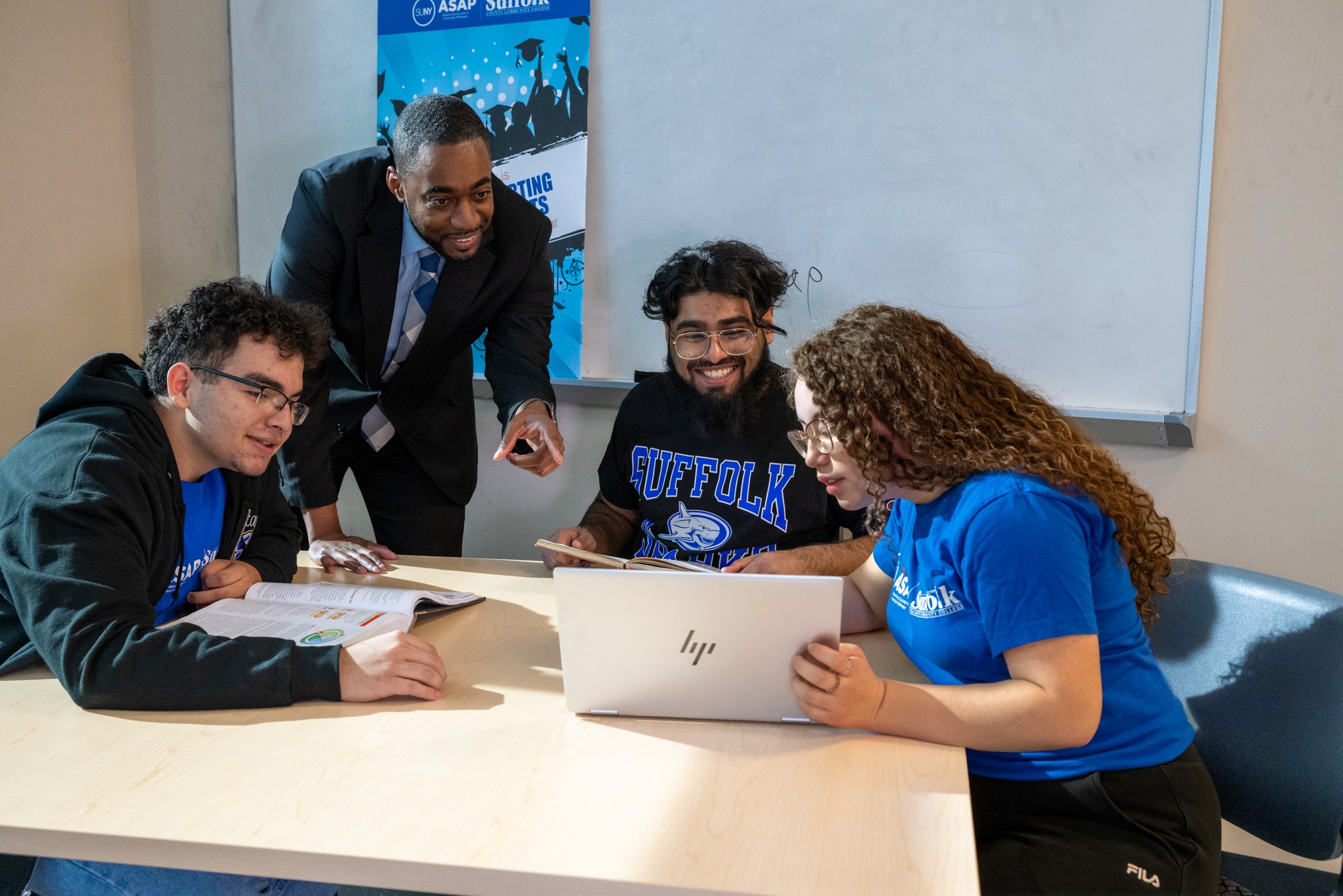 Three Suffolk students with an advisor discussing something on a laptop